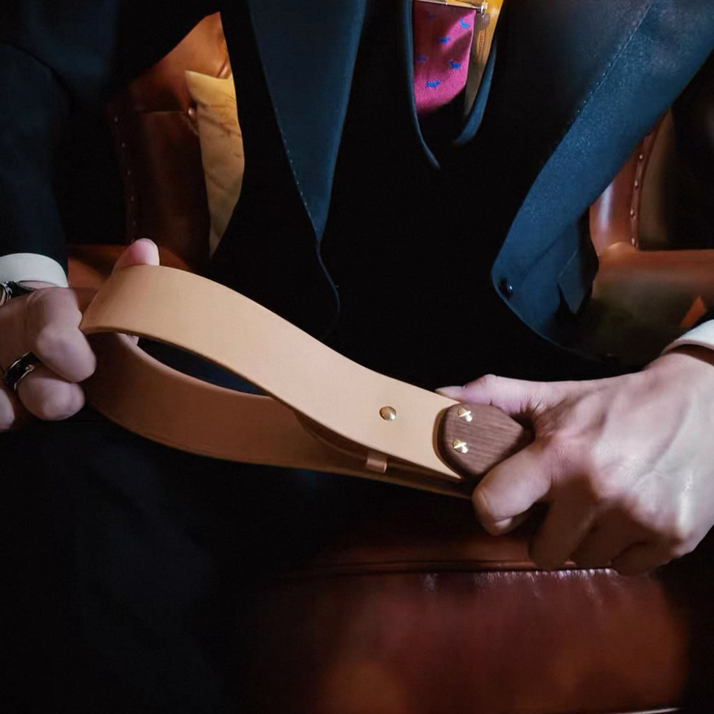 Natural leather paddle held in both hands by suited male model – walnut handle BDSM impact play lifestyle editorial
