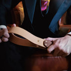 Natural leather paddle held in both hands by suited male model – walnut handle BDSM impact play lifestyle editorial
