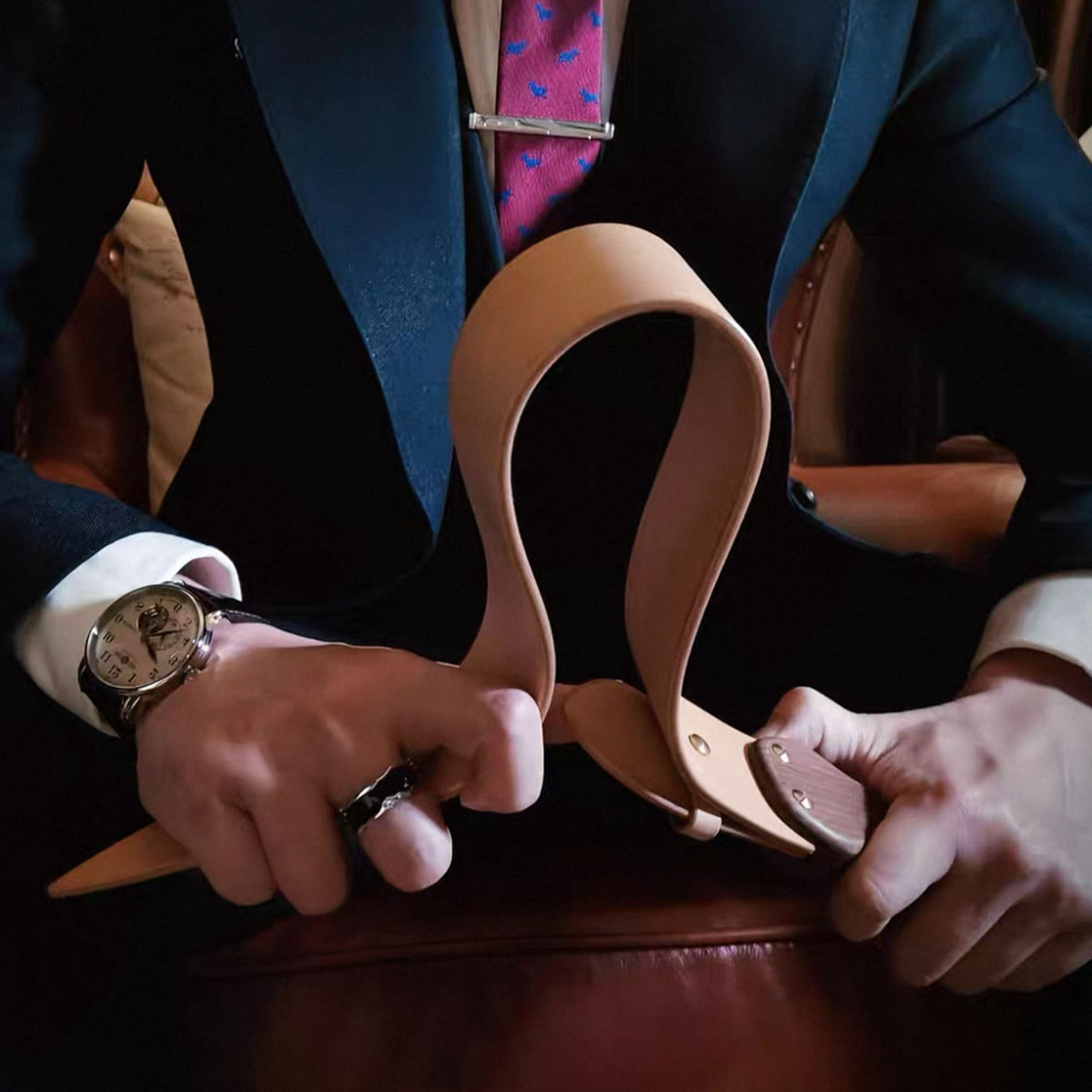 Natural leather paddle flexed in both hands by suited model – walnut handle cowhide BDSM lifestyle editorial
