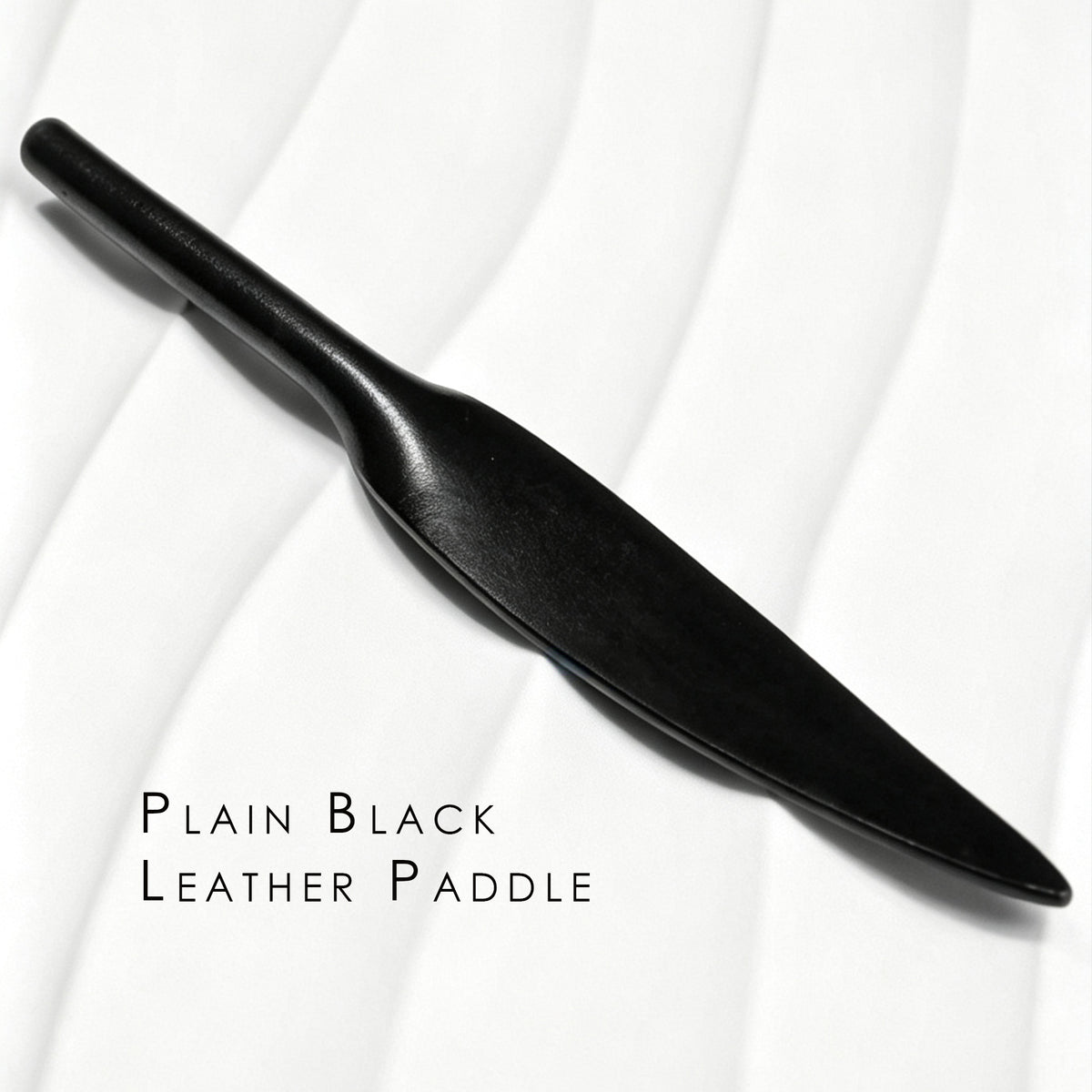 Plain black leather paddle on white background – smooth leaf blade tapered handle one-piece cowhide BDSM portable paddle
