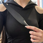 Plain black leather paddle held against chest by model in black hoodie – leaf tip upward tapered handle BDSM lifestyle editorial
