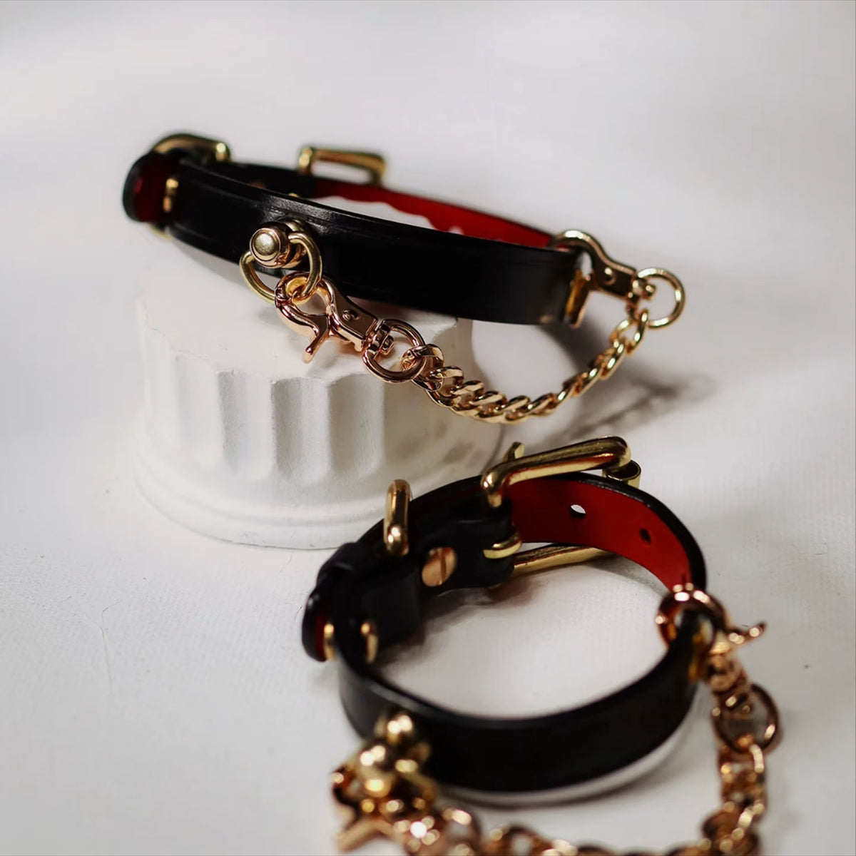 Black red leather BDSM collar and wrist cuffs stacked on display stand – gold hardware chain leash red lining set
