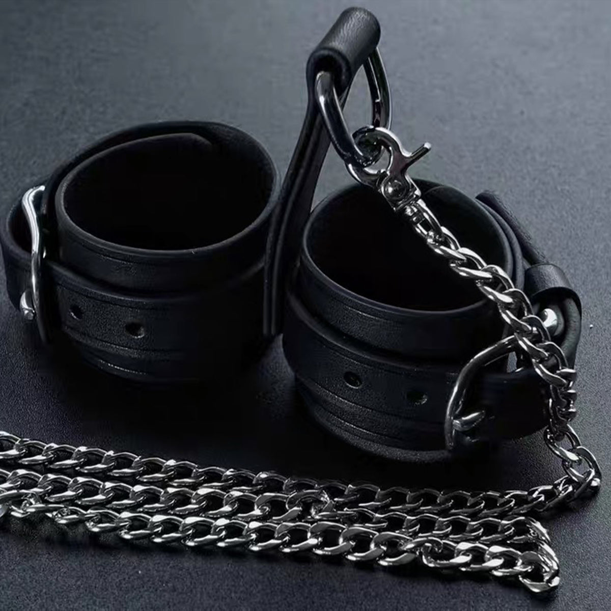 Black leather wrist cuffs pair with silver chain leash flat lay – buckle D-ring connector full set display

