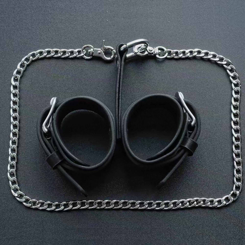 Black leather wrist cuffs pair overhead flat lay – silver chain leash surrounding full set product layout
