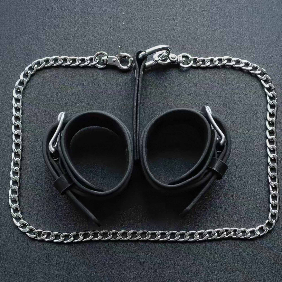 Black leather wrist cuffs pair overhead flat lay – silver chain leash surrounding full set product layout
