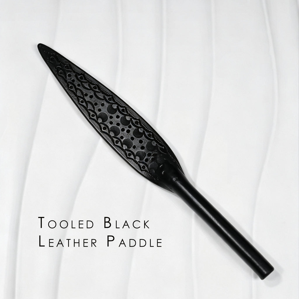 Black tooled leather paddle product display – intricate carved floral pattern leaf blade tapered handle BDSM handmade ShadowedBodies
