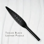 Black tooled leather paddle product display – intricate carved floral pattern leaf blade tapered handle BDSM handmade ShadowedBodies
