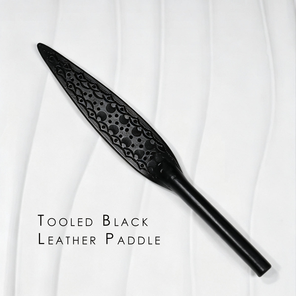 Black tooled leather paddle product display – intricate carved floral pattern leaf blade tapered handle BDSM handmade ShadowedBodies
