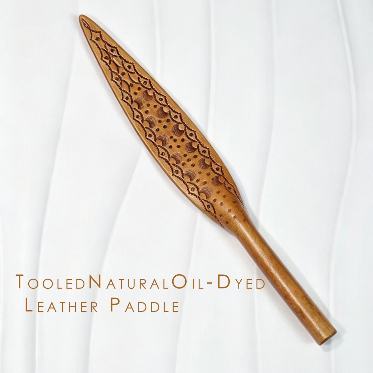 Natural oil-dyed tooled leather paddle on white background – intricate carved floral pattern leaf blade full view BDSM handmade
