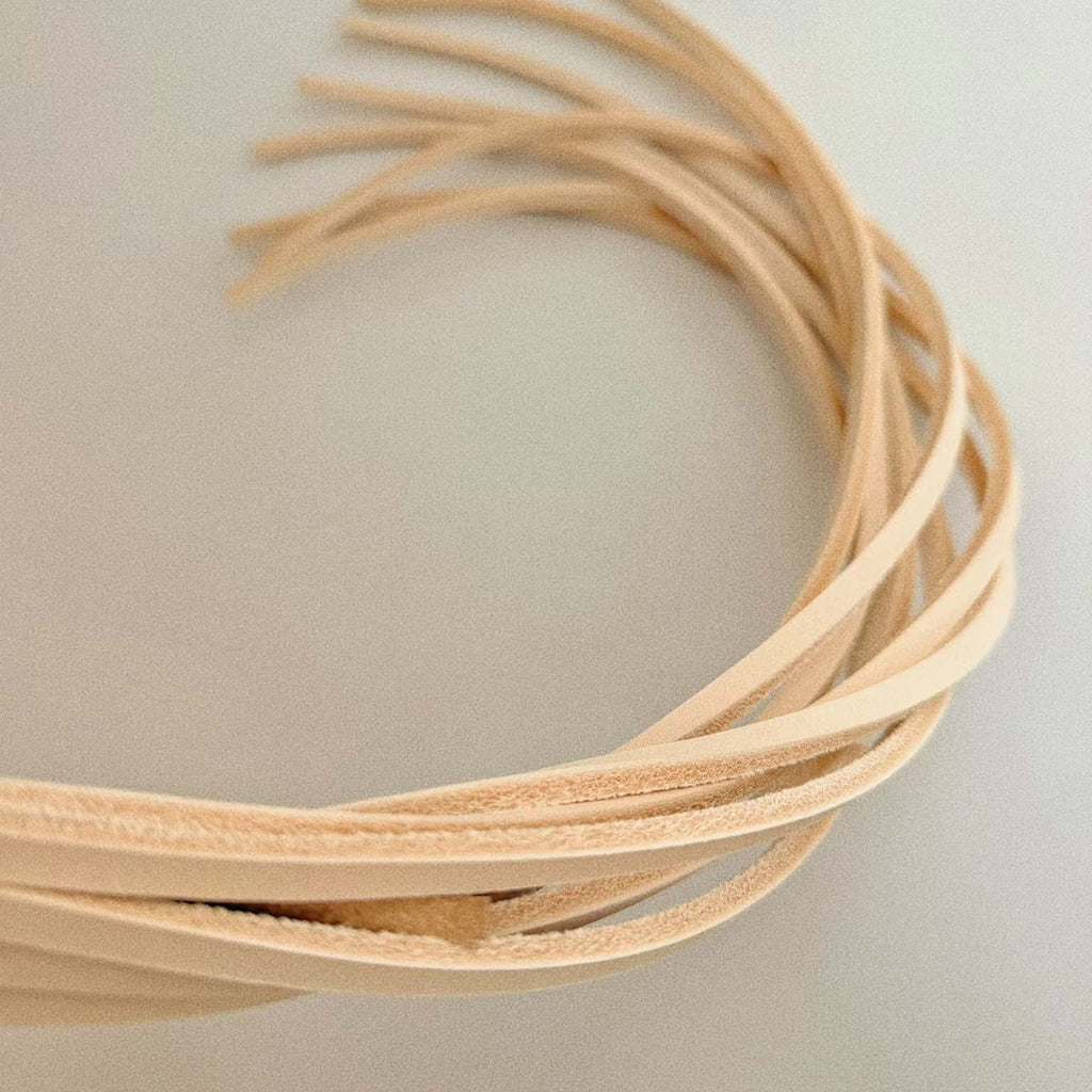Natural vegetable tanned leather flogger tails looped close-up on gray surface – cream strap edges textured tips splayed BDSM detail
