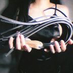 Black leather flogger held by model – walnut wood handle BDSM impact play lifestyle editorial handmade
