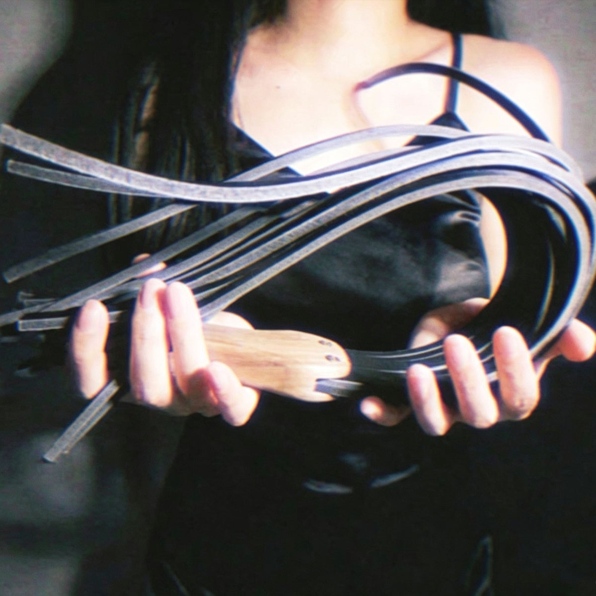 Black leather flogger held by model – walnut wood handle BDSM impact play lifestyle editorial handmade

