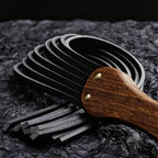 Black leather flogger handle and tails close-up on dark textured surface – walnut grain gold rivet vegetable tanned detail BDSM
