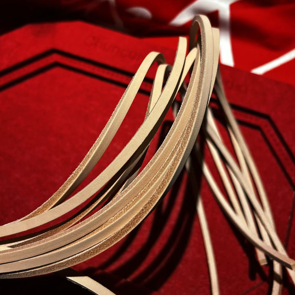 Natural vegetable tanned leather flogger tails arched close-up on red velvet – grain and flesh side texture detail BDSM artisan craft
