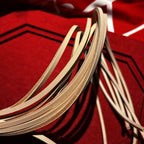 Natural vegetable tanned leather flogger tails arched close-up on red velvet – grain and flesh side texture detail BDSM artisan craft
