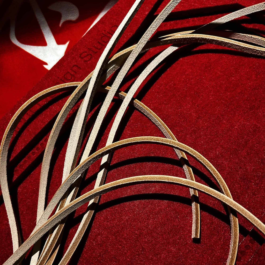 Natural leather flogger tails tangled close-up on red velvet surface – cream vegetable tanned strap texture contrast dramatic BDSM detail
