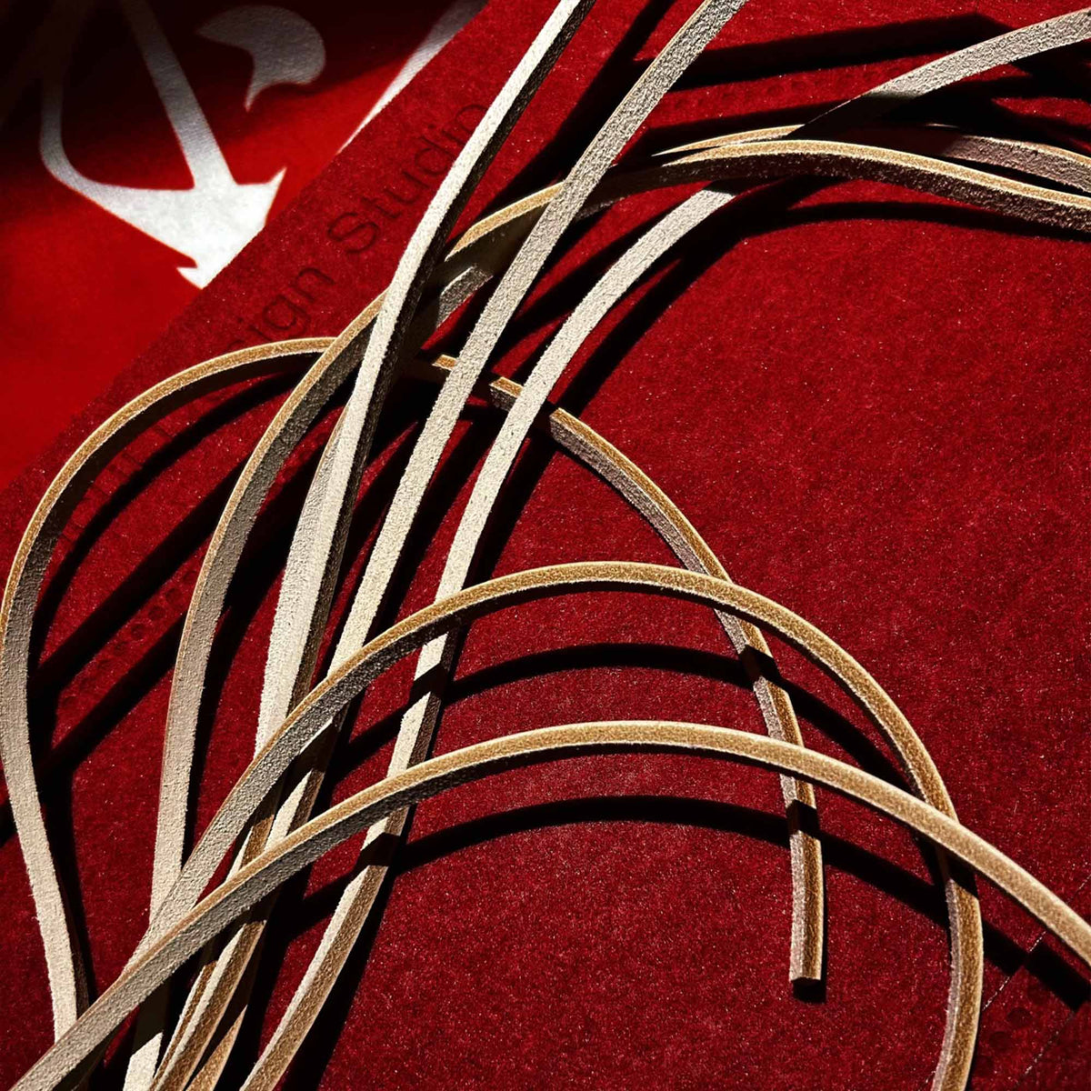Natural leather flogger tails tangled close-up on red velvet surface – cream vegetable tanned strap texture contrast dramatic BDSM detail
