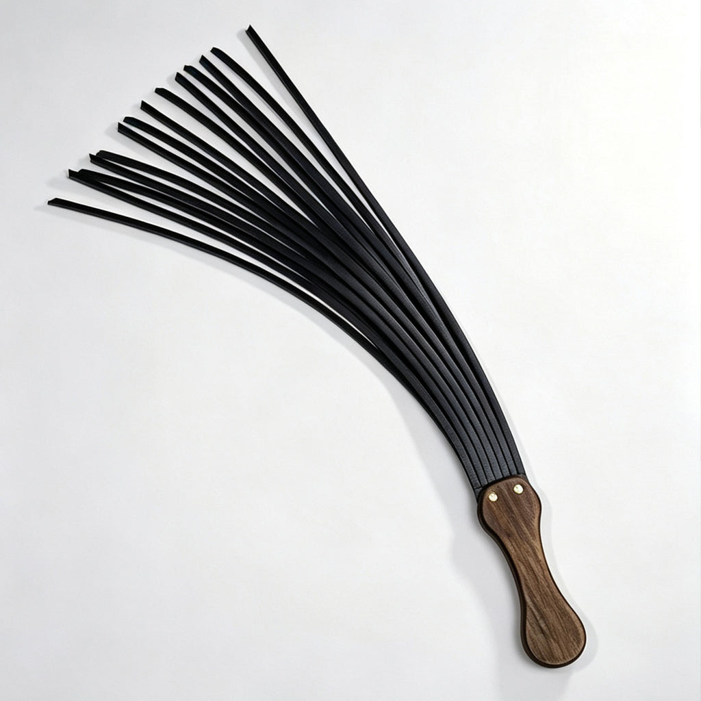 Black leather flogger flat lay on white background – multiple tails fanned out walnut handle gold rivet full view BDSM
