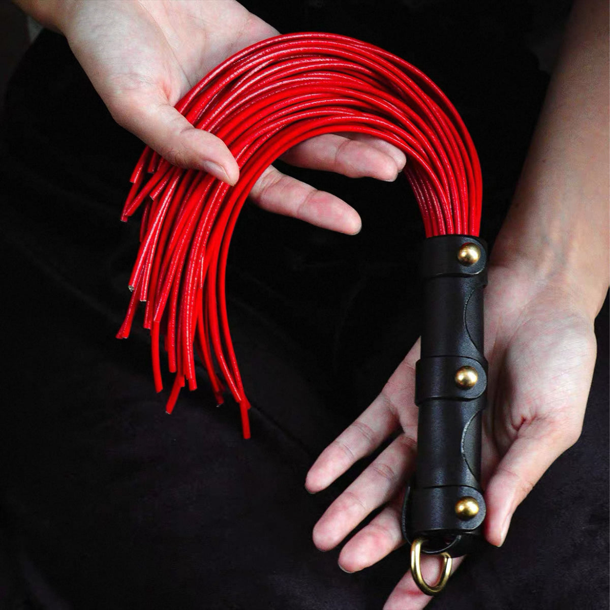 Red leather whip front view held in both hands – black handle gold rivets O-ring red lash vegetable tanned cowhide
