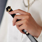 Black leather whip handle close-up held in hand – gold D-ring rivet tip detail full grain cowhide BDSM crop
