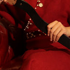 Black leather paddle held against red-dressed model – walnut wood handle gold rivet BDSM impact play lifestyle scene
