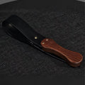 Black leather paddle with walnut wood handle product display – gold rivet cowhide BDSM impact play handmade ShadowedBodies

