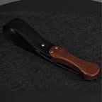 Black leather paddle with walnut wood handle product display – gold rivet cowhide BDSM impact play handmade ShadowedBodies
