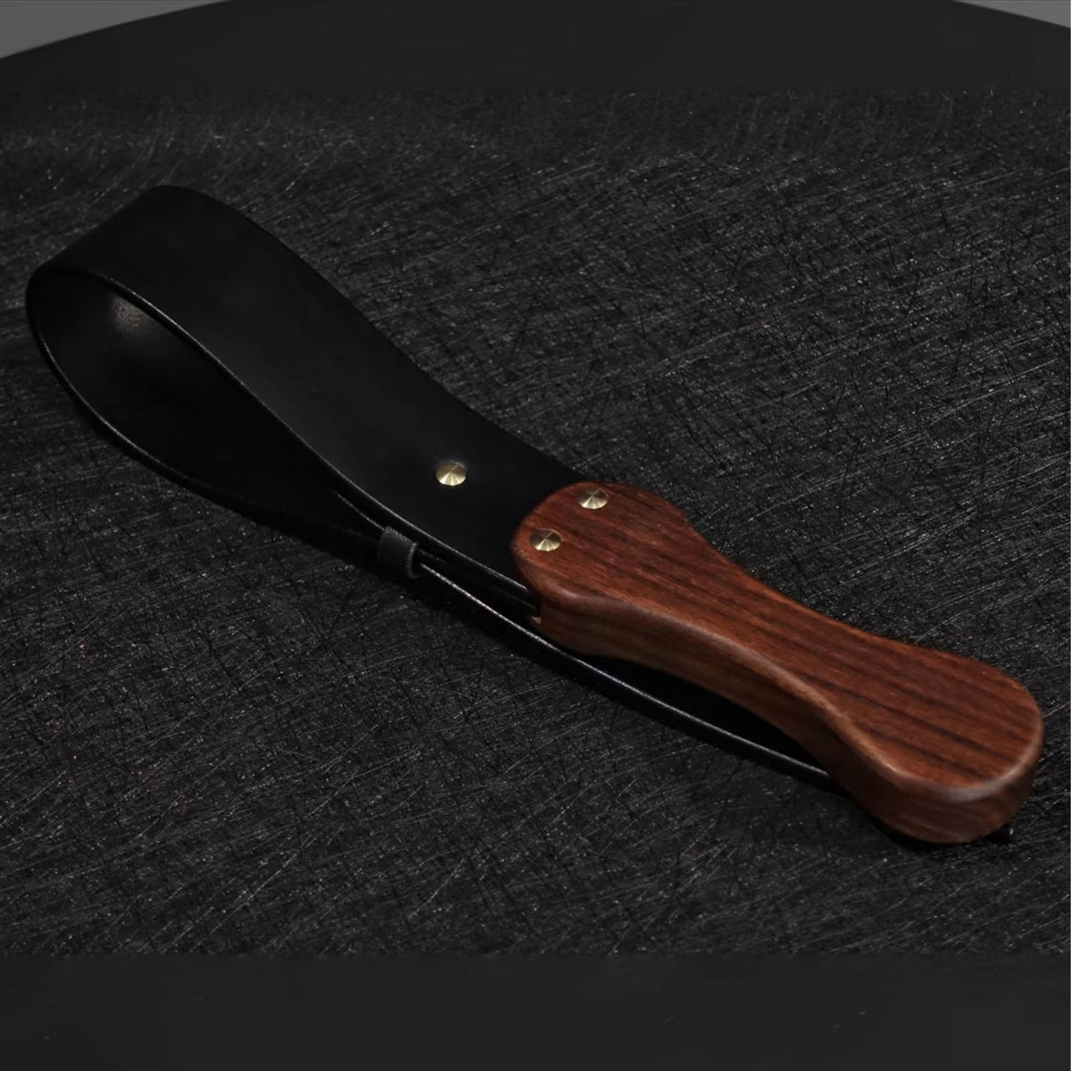 Black leather paddle with walnut wood handle product display – gold rivet cowhide BDSM impact play handmade ShadowedBodies
