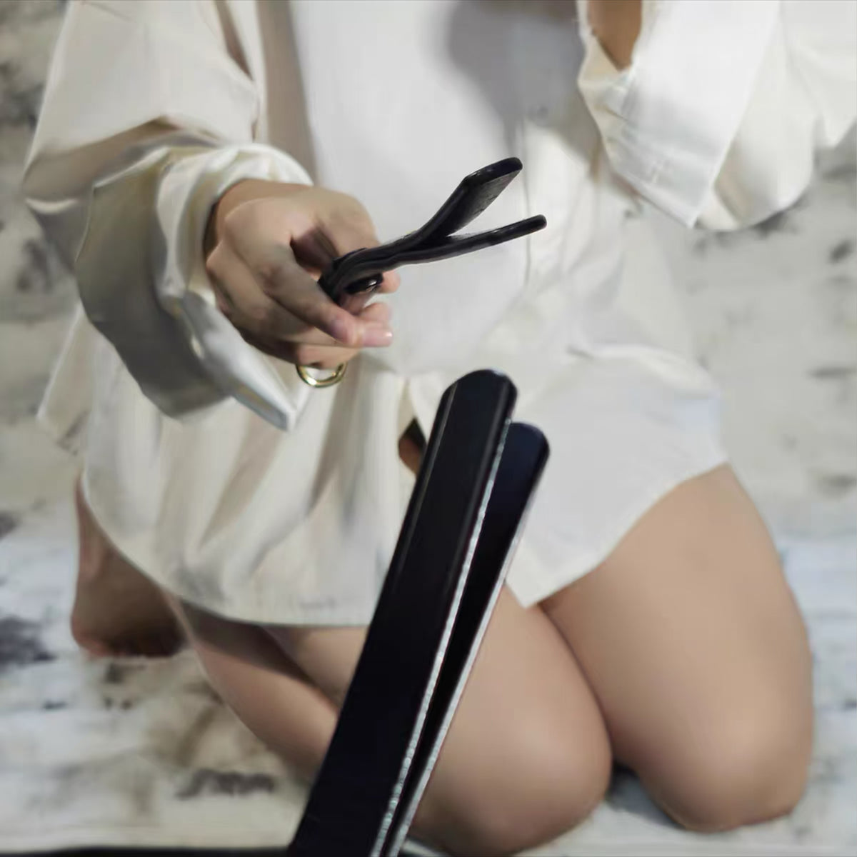 Black leather whip held at midsection by model both hands – split tip toward camera BDSM crop lifestyle scene
