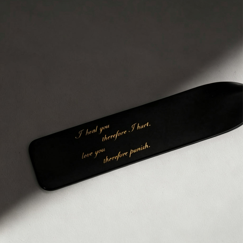 Black leather riding crop custom engraving close-up – gold script personalized text BDSM impact play detail
