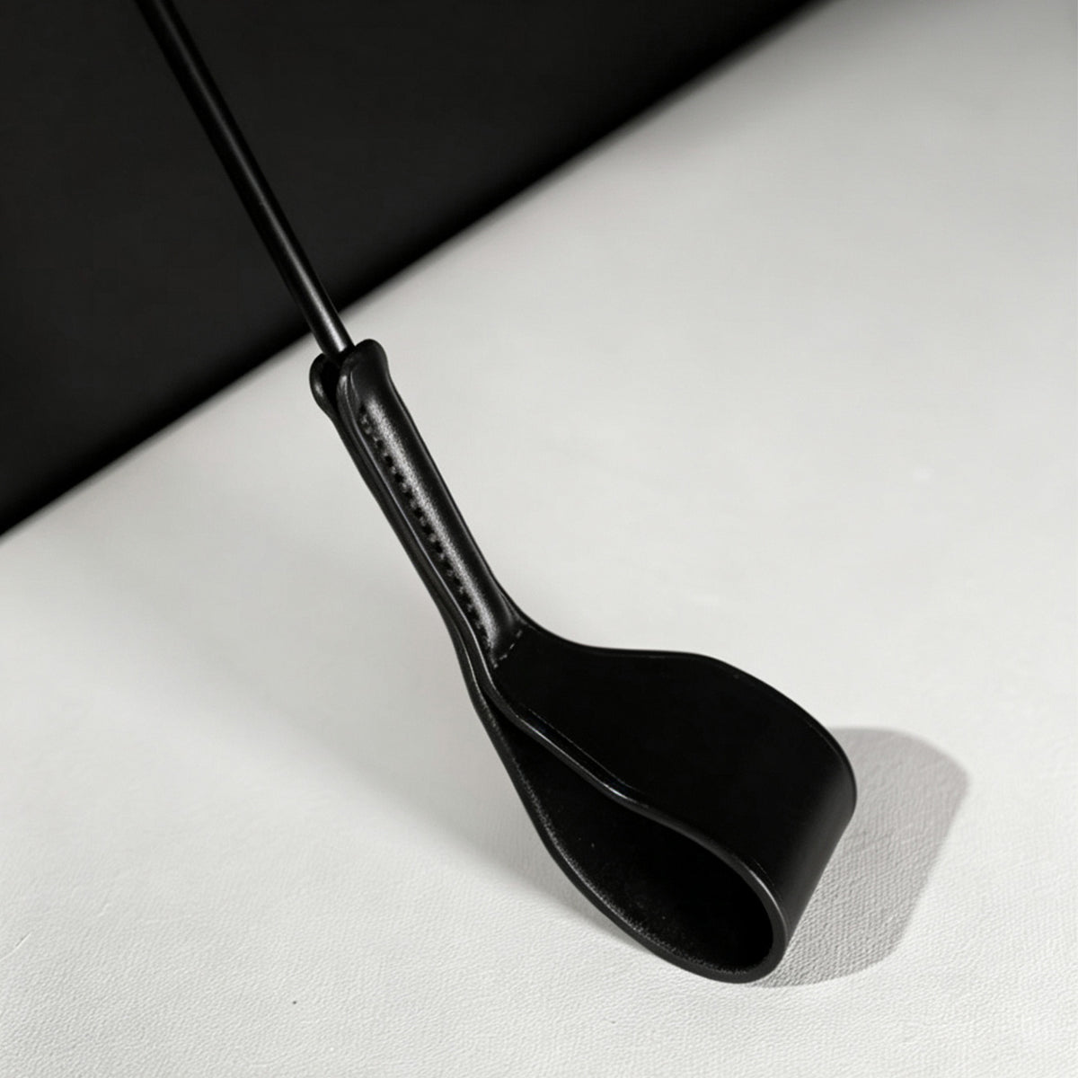 Black leather riding crop folded tip close-up – stitched neck connection vegetable tanned detail BDSM crop
