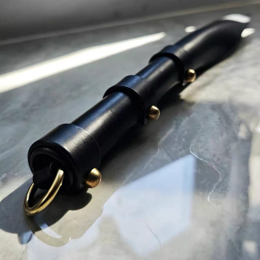 Black leather soft paddle handle close-up on marble surface – segmented wrap gold rivet D-ring detail cowhide BDSM
