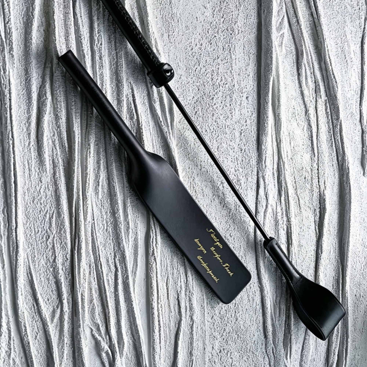 Black leather paddle and riding crop displayed together – vegetable tanned handmade BDSM impact play set product display
