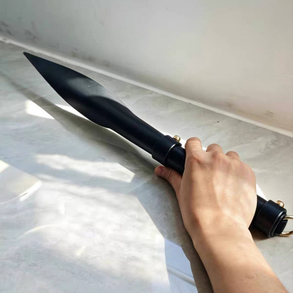 Black leather soft paddle gripped in hand tip pointing up – leaf shaped blade segmented handle gold rivet BDSM impact play

