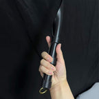 Black leather soft paddle handle gripped in hand against black background – segmented leather wrap gold D-ring cowhide detail
