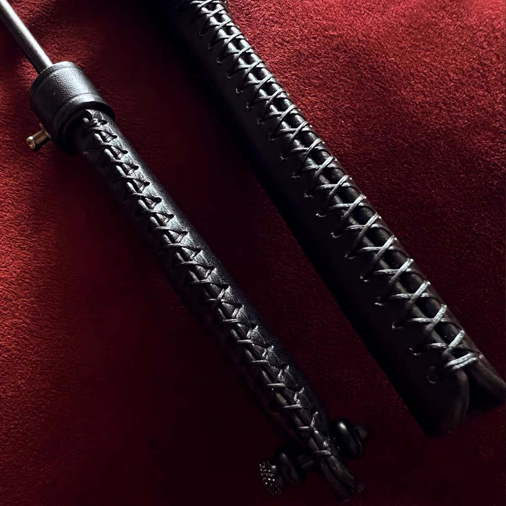 Black leather riding crop handle cross-stitch detail on red velvet – two crops handmade craftsmanship close-up
