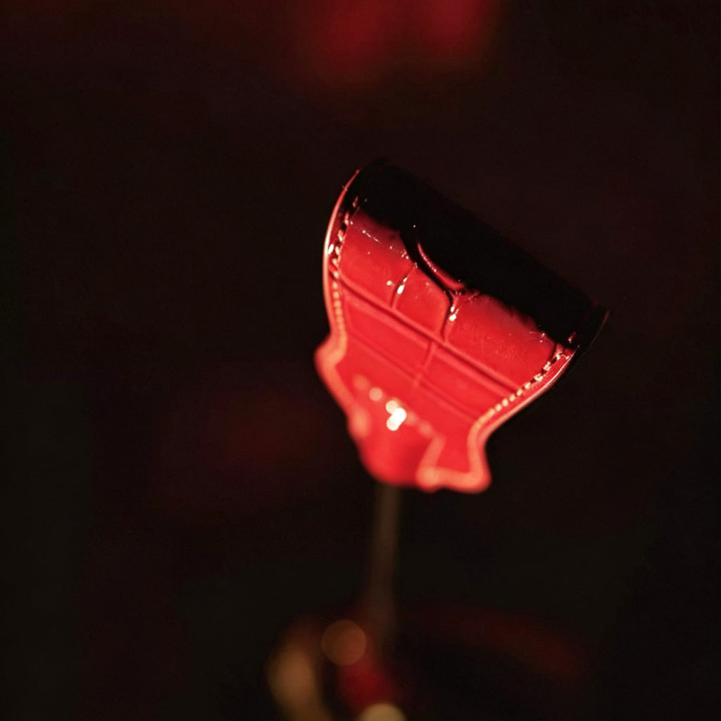 Red patent crocodile leather crop tip close-up from below – glossy embossed texture white stitch dramatic red light BDSM detail
