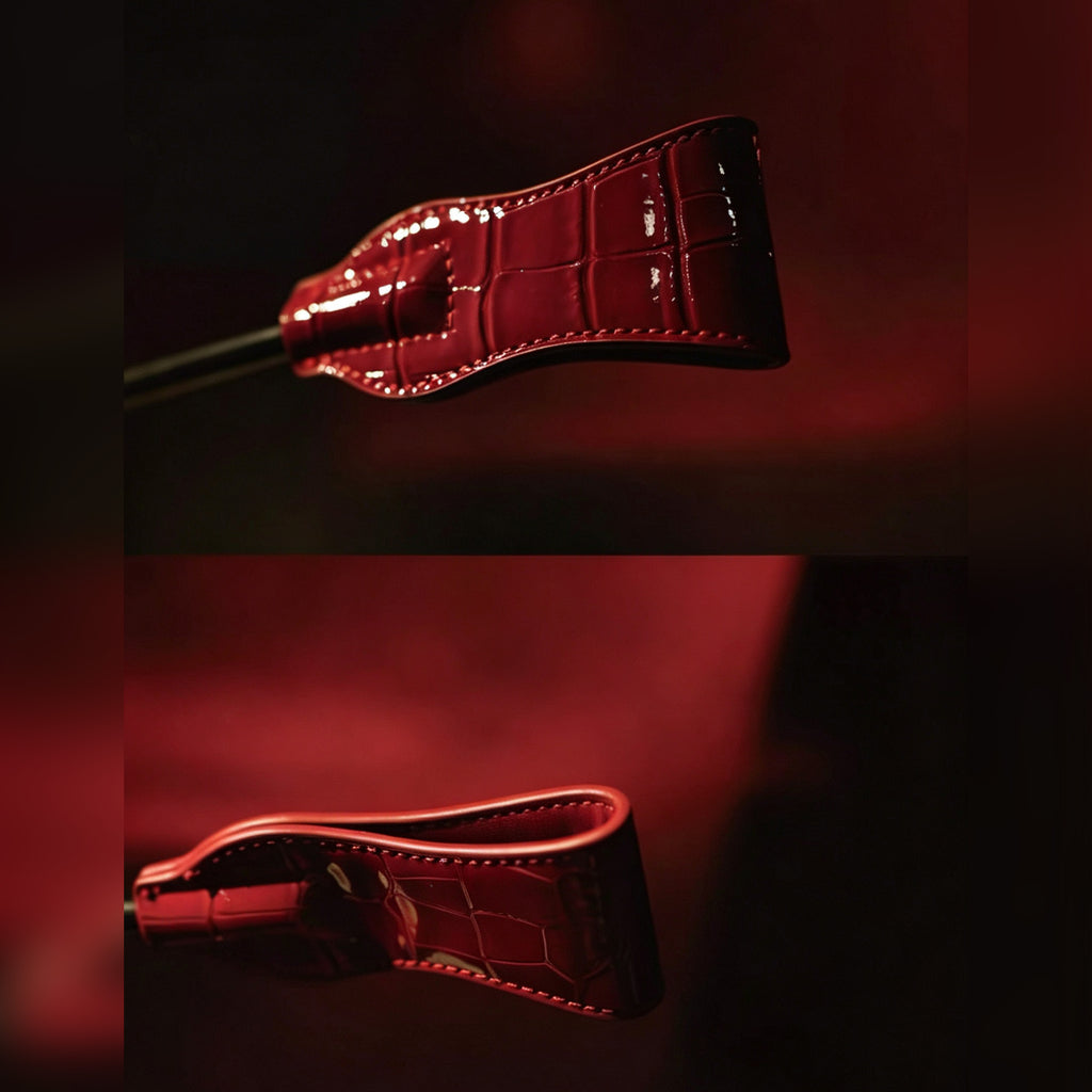 Red patent crocodile-embossed leather crop tip detail – side and front view white saddle stitch glossy texture BDSM close-up
