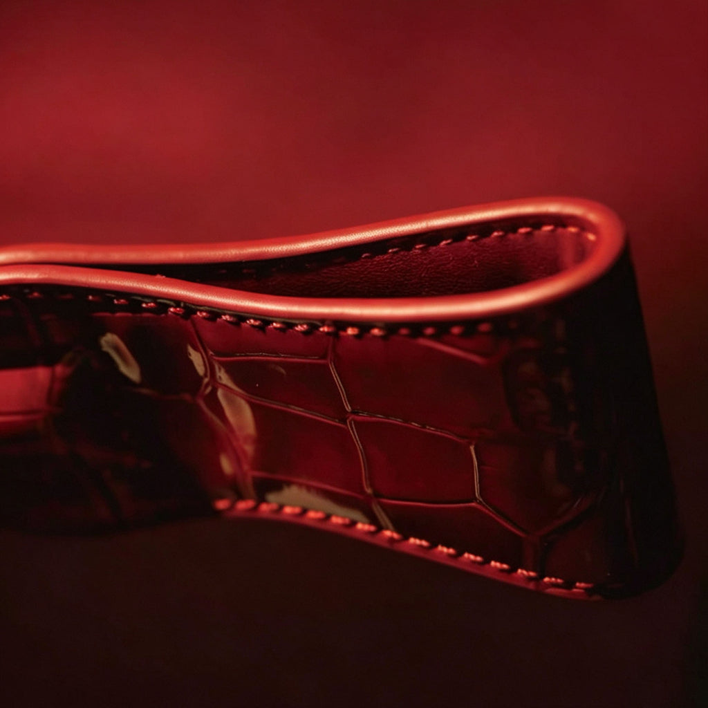 Red patent crocodile leather crop paddle close-up on dark red surface – folded edge saddle stitch glossy embossed texture BDSM

