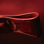 Red patent crocodile leather crop paddle close-up on dark red surface – folded edge saddle stitch glossy embossed texture BDSM
