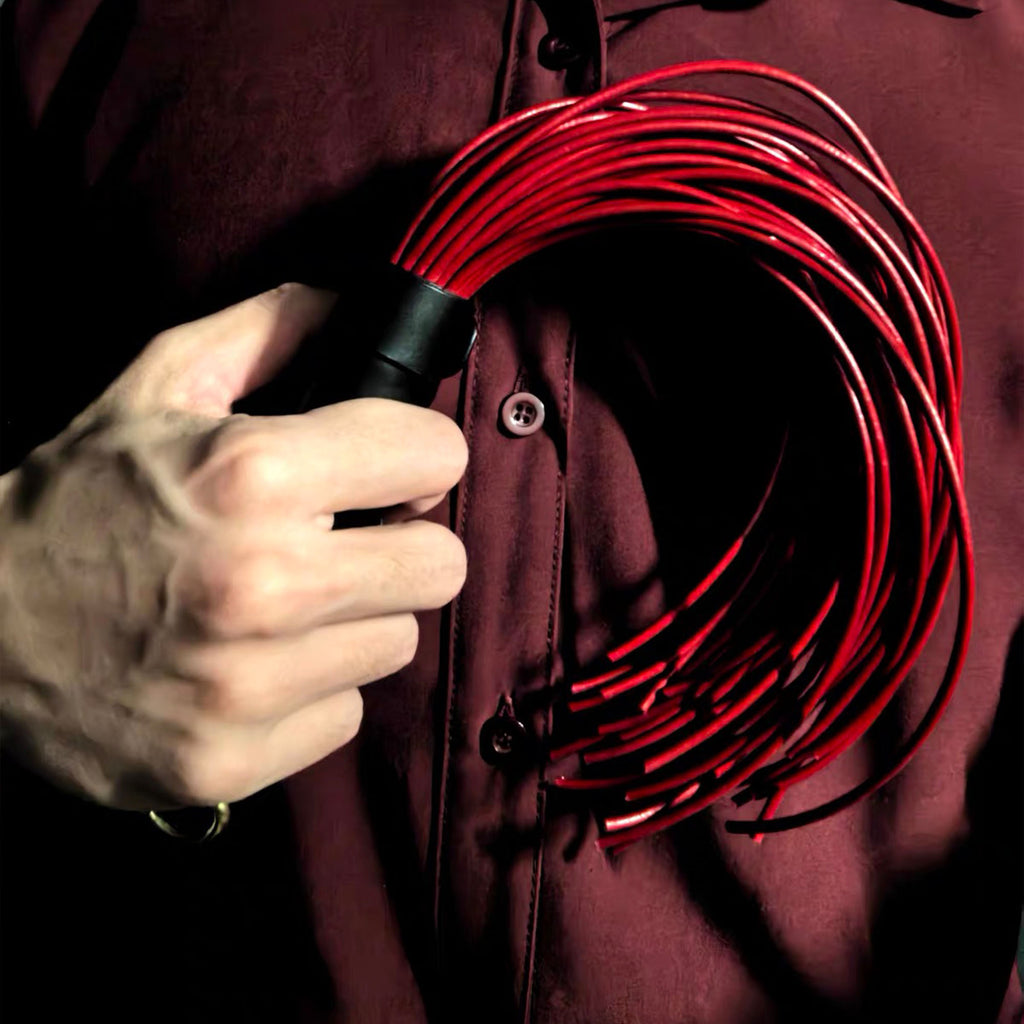 Red leather whip gripped in hand against dark shirt – black handle red lash coil BDSM impact play editorial
