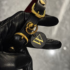 Red leather spiked choker held in black gloved hands – gold buckle O-ring ShadowedBodies brand tag custom charm
