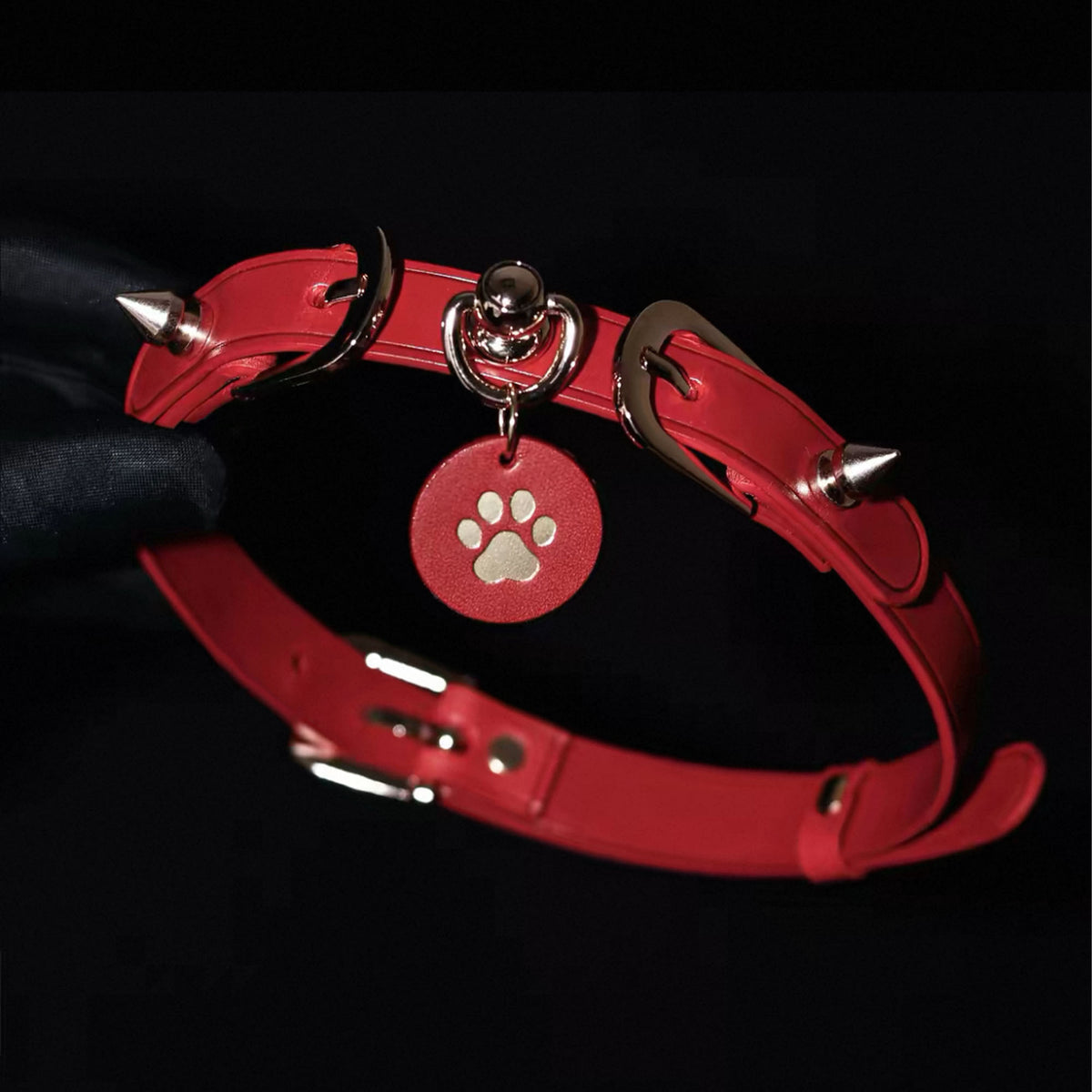 Red leather spiked choker hardware detail hand-held – gold buckle O-ring cone spike rivet custom pendant close-up
