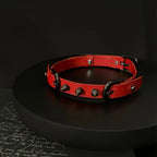Matte red leather BDSM choker on black display stand – black cone spike rivets double buckle dark editorial
