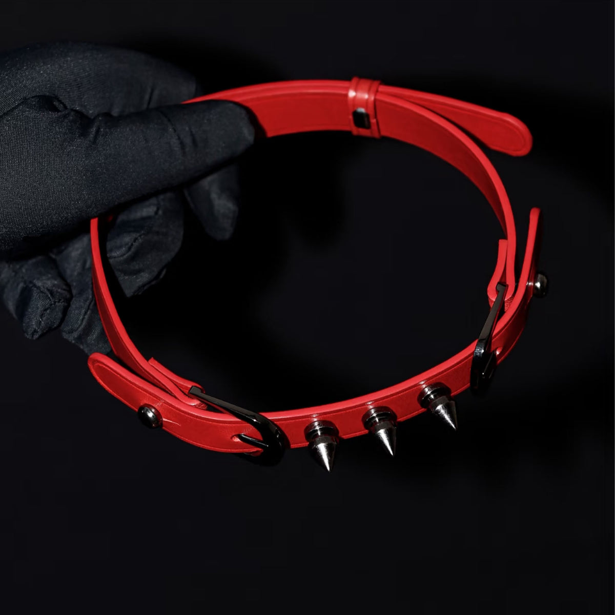 Matte red leather spiked BDSM choker hand-held overhead view – silver cone rivets black hardware double buckle
