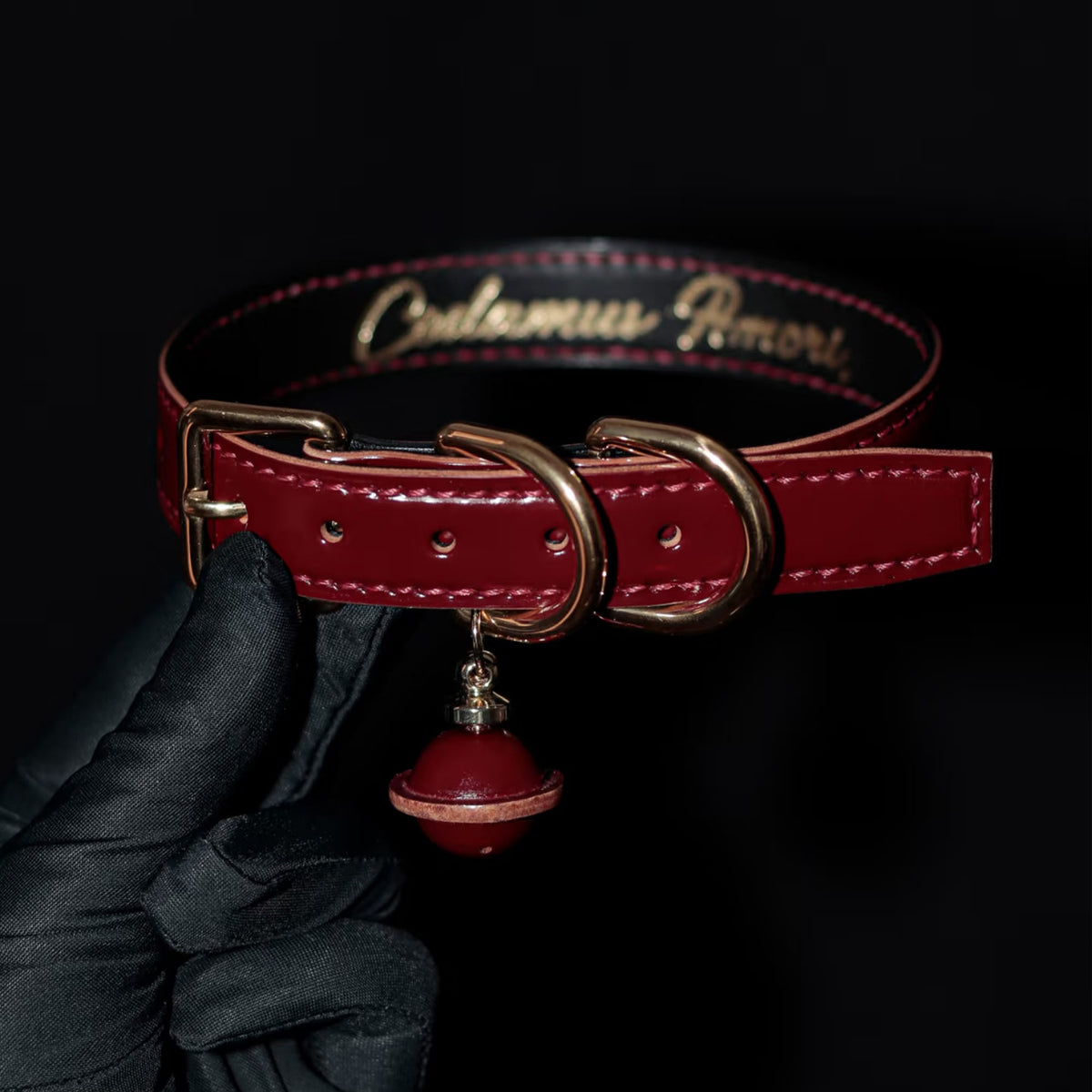 Burgundy leather BDSM collar front view – red lacquer bell pendant gold hardware hand-stitched ShadowedBodies
