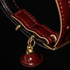 Burgundy leather collar interior close-up – red hand stitching gold connector red bell pendant craftsmanship detail
