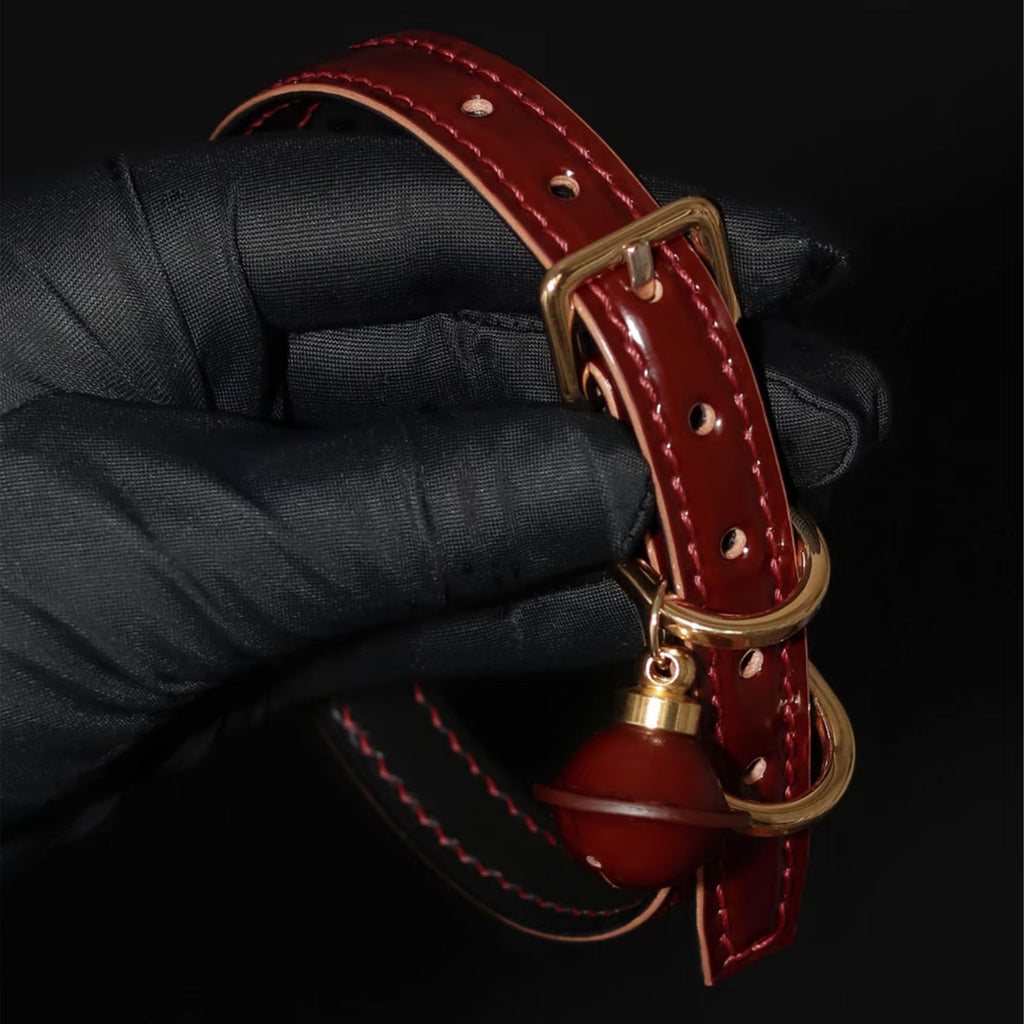 Burgundy leather BDSM collar hand-held – gold square buckle red bell pendant glossy leather surface detail
