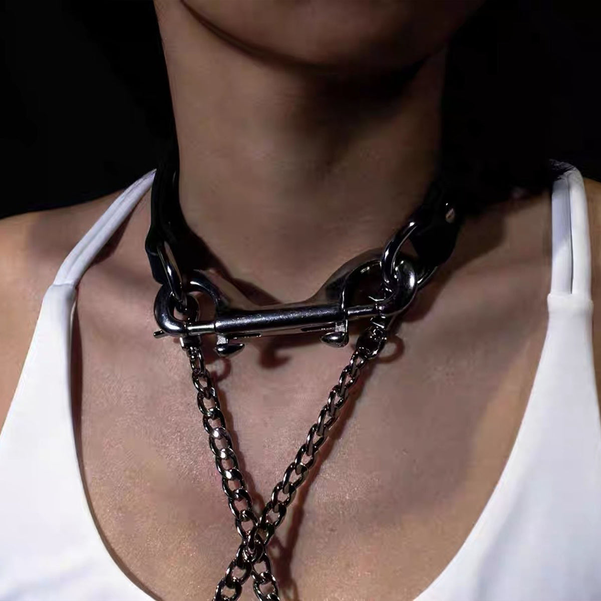 Detailed close-up of model wearing black leather collar connected horizontally with a silver double bolt snap and chain detail