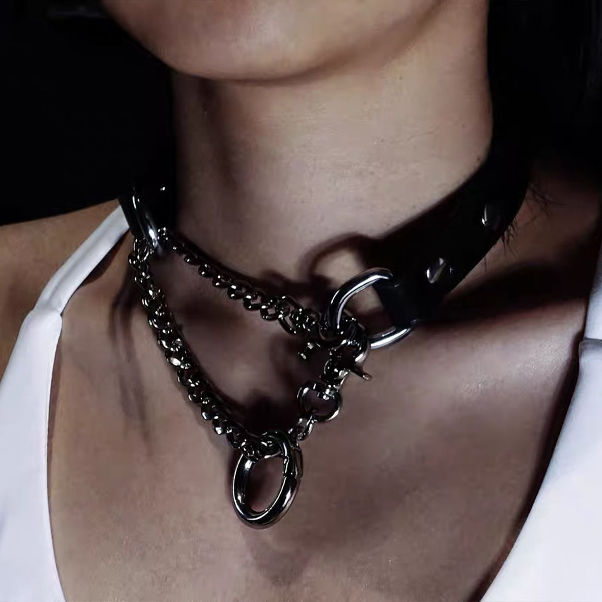 Close-up angle of model wearing black leather collar with asymmetrical draped silver curb chains and ring connector
